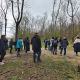 A group of individuals on a nature walk in a wooded area during the colder months, with leafless trees and a cloudy sky above