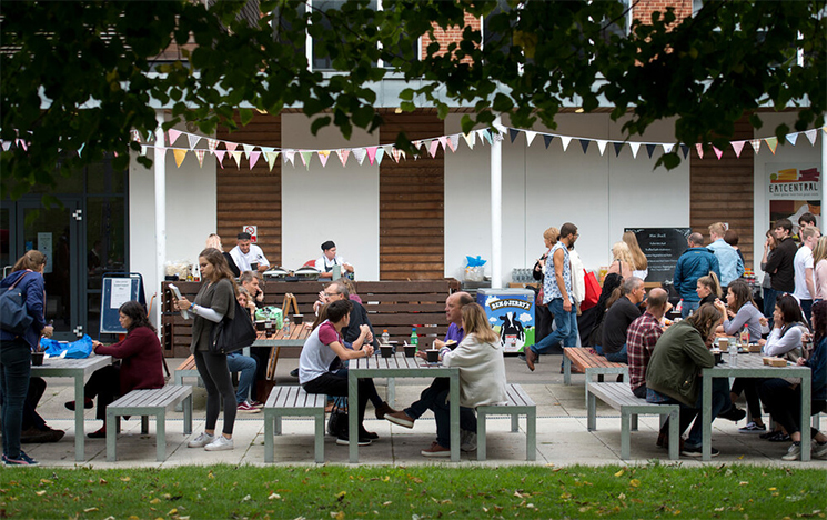 Students sitting outside by Eat Central eating food at the picnic tables provided